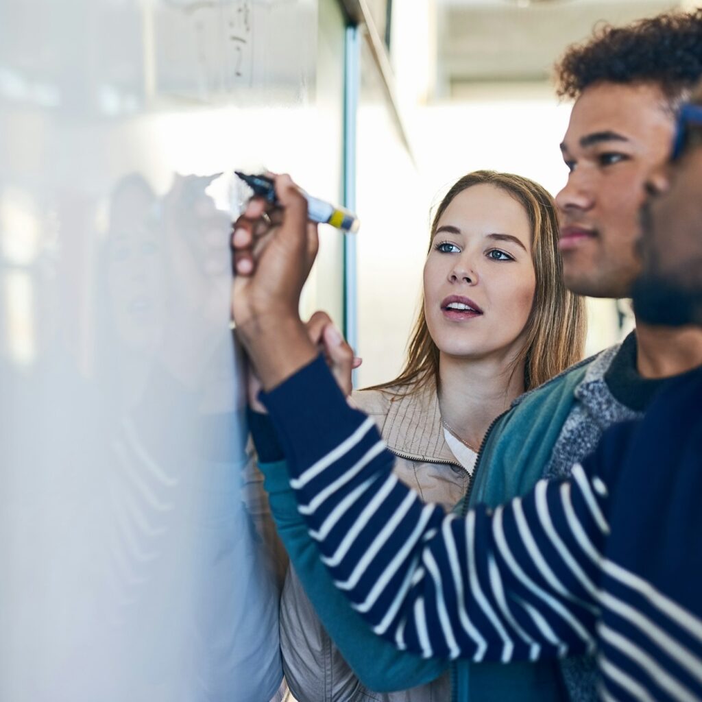 Sharing an important technique. Shot of a young man writing on a whiteboard while students look on.